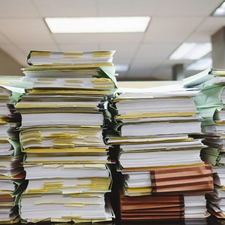 Bürokratie Mehrere Aktenstapel, die sich in einem Büro türmen.
